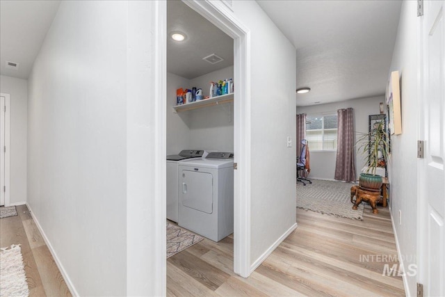 clothes washing area with light wood-type flooring, washing machine and dryer, and baseboards