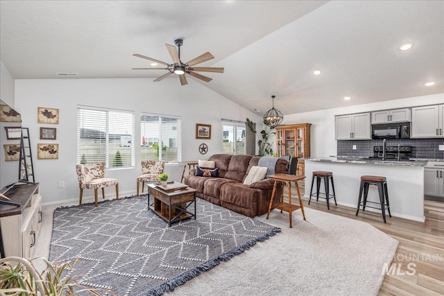 living room with ceiling fan, lofted ceiling, a chandelier, recessed lighting, and light wood-style flooring