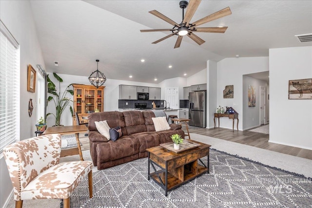 living area featuring lofted ceiling, a ceiling fan, light wood-style flooring, a chandelier, and recessed lighting