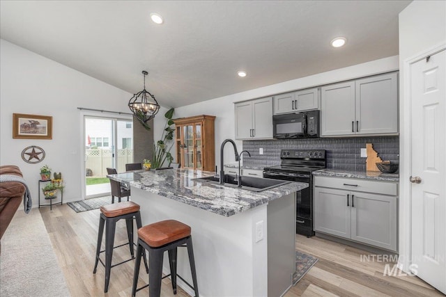 kitchen featuring black appliances, gray cabinetry, a sink, lofted ceiling, and backsplash