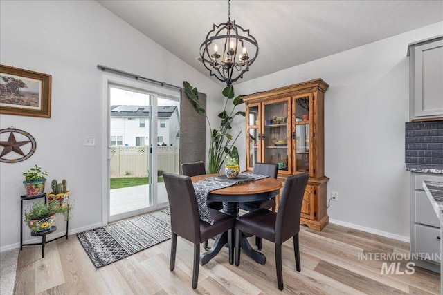 dining area with a chandelier, light wood-style flooring, vaulted ceiling, and baseboards