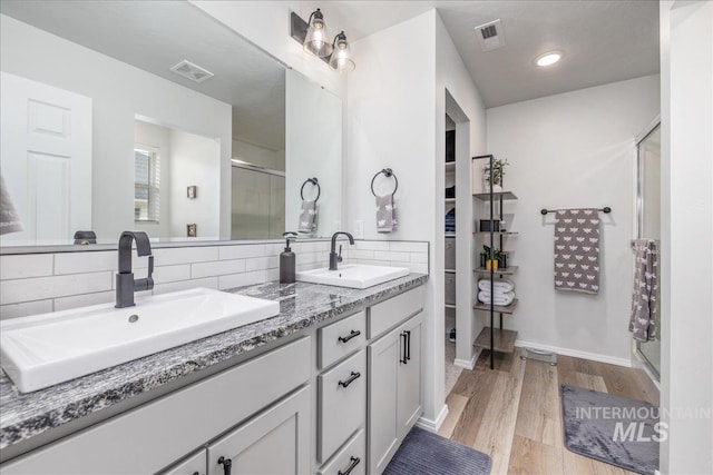 bathroom featuring a shower stall, tasteful backsplash, wood finished floors, and double vanity