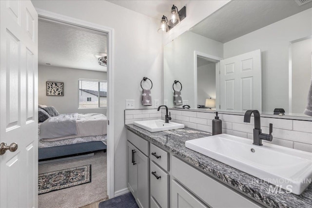bathroom featuring ensuite bath, double vanity, tasteful backsplash, and a textured ceiling