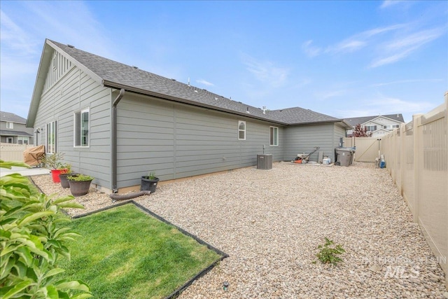 rear view of property featuring a fenced backyard, board and batten siding, central AC unit, and roof with shingles