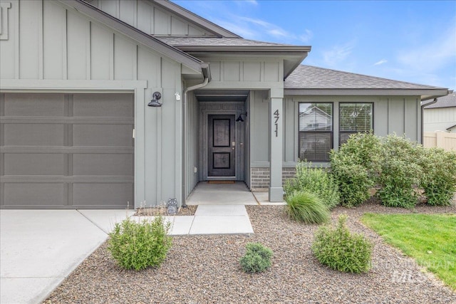view of exterior entry featuring roof with shingles, an attached garage, board and batten siding, and concrete driveway