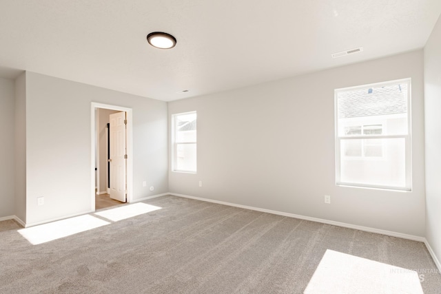 spare room featuring light carpet, visible vents, and baseboards