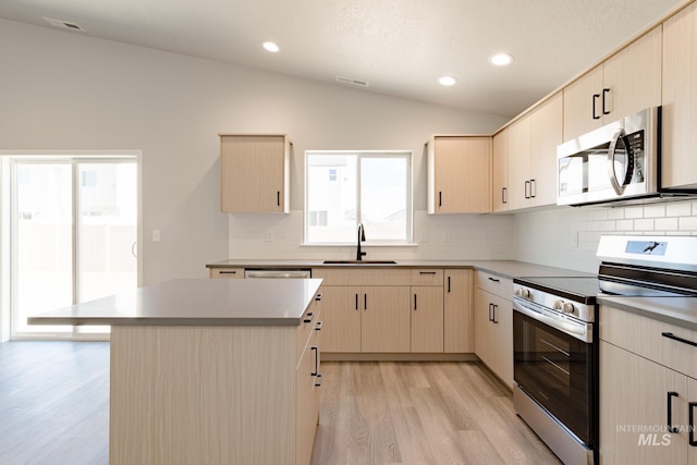 kitchen featuring visible vents, light wood finished floors, a sink, vaulted ceiling, and appliances with stainless steel finishes