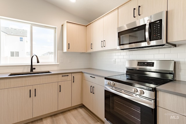 kitchen with light wood-style flooring, light brown cabinets, a sink, tasteful backsplash, and stainless steel appliances