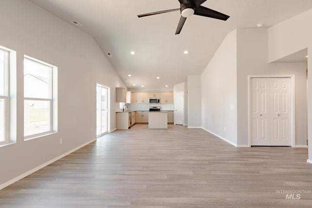 unfurnished living room with baseboards, high vaulted ceiling, ceiling fan, a sink, and light wood-type flooring