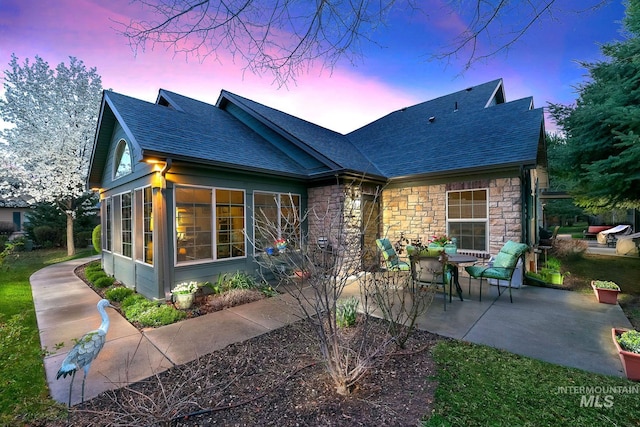 2870 N Cloverdale, Boise, ID 83713 - back of house at dusk with a patio area, a sunroom, a shingled roof, and stone siding