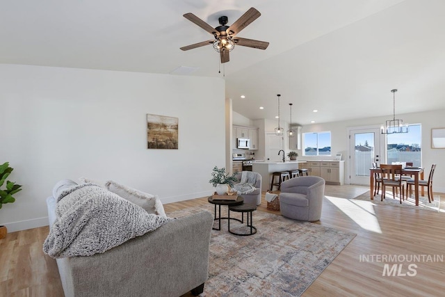 living area with ceiling fan with notable chandelier, recessed lighting, light wood finished floors, baseboards, and vaulted ceiling