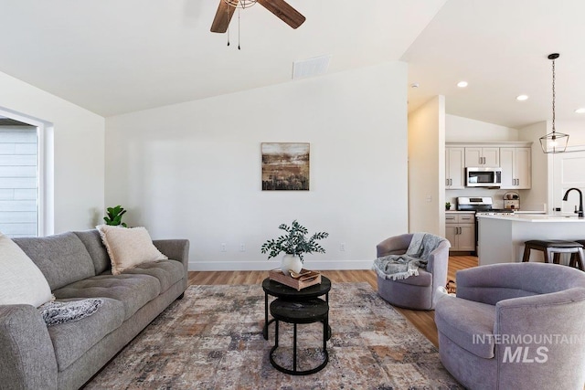 living room featuring baseboards, visible vents, light wood finished floors, ceiling fan, and vaulted ceiling