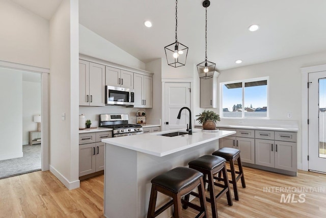 kitchen featuring gray cabinetry, light countertops, a kitchen bar, appliances with stainless steel finishes, and a sink