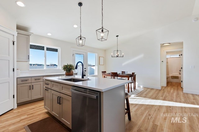 kitchen with a sink, light countertops, pendant lighting, stainless steel dishwasher, and light wood-type flooring