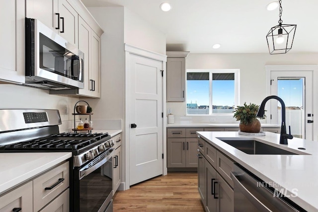 kitchen featuring gray cabinetry, pendant lighting, light countertops, appliances with stainless steel finishes, and a sink