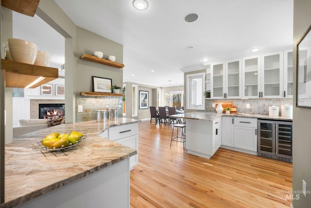 kitchen featuring beverage cooler, a peninsula, a glass covered fireplace, white cabinets, and open shelves