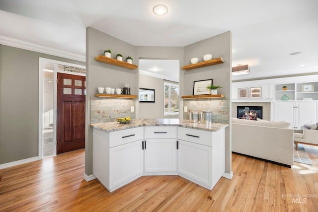 kitchen featuring light wood finished floors, light stone countertops, crown molding, and open shelves