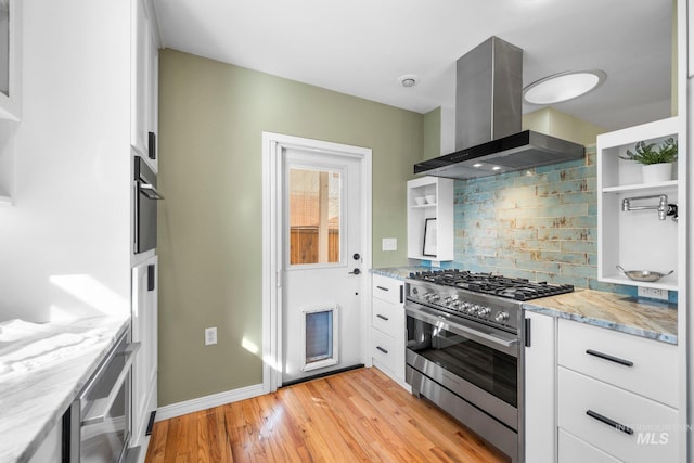 kitchen featuring high end stove, backsplash, white cabinetry, light wood-style floors, and wall chimney exhaust hood