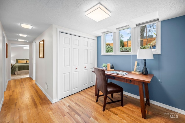 office space with light wood-type flooring, baseboards, and a textured ceiling