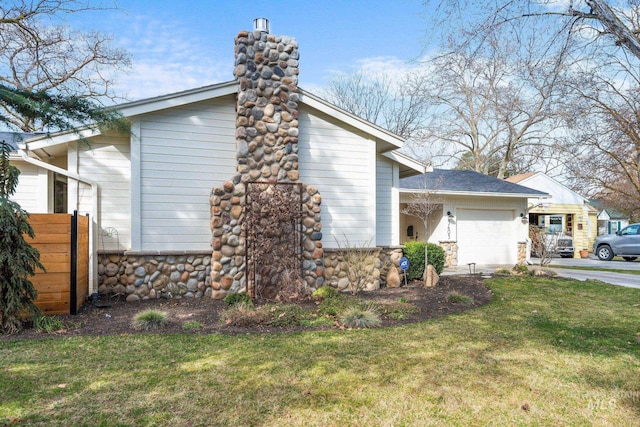 view of side of property with a lawn, stone siding, concrete driveway, a garage, and a chimney