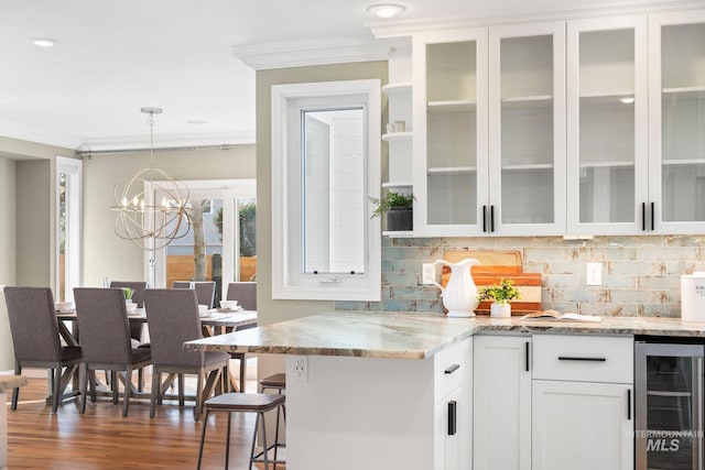 kitchen with beverage cooler, backsplash, white cabinetry, and ornamental molding