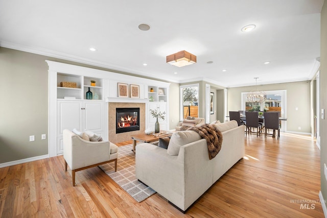 living area with a tiled fireplace, crown molding, baseboards, and light wood-type flooring