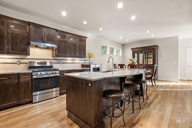 kitchen featuring light wood-style flooring, a breakfast bar area, under cabinet range hood, a sink, and gas stove