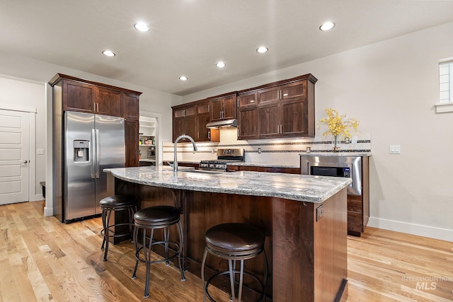 kitchen with appliances with stainless steel finishes, light wood-style floors, under cabinet range hood, and decorative backsplash