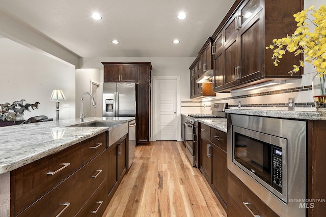 kitchen with under cabinet range hood, a sink, appliances with stainless steel finishes, light stone countertops, and light wood finished floors