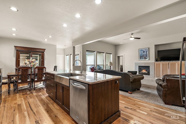 kitchen with open floor plan, dark brown cabinets, light wood-type flooring, stainless steel dishwasher, and a sink