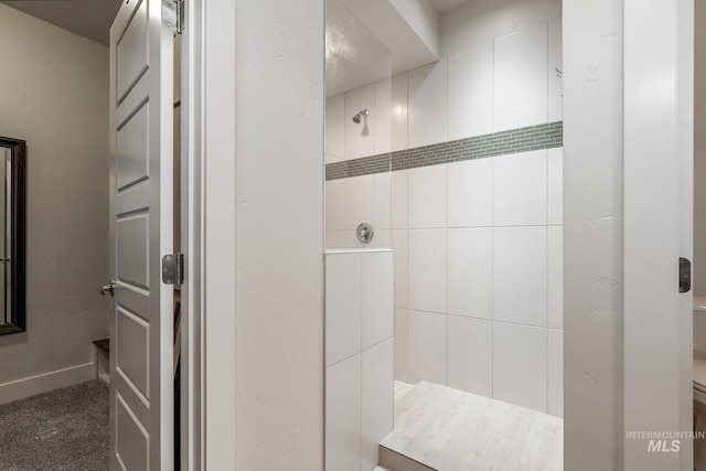 full bathroom featuring tiled shower and baseboards