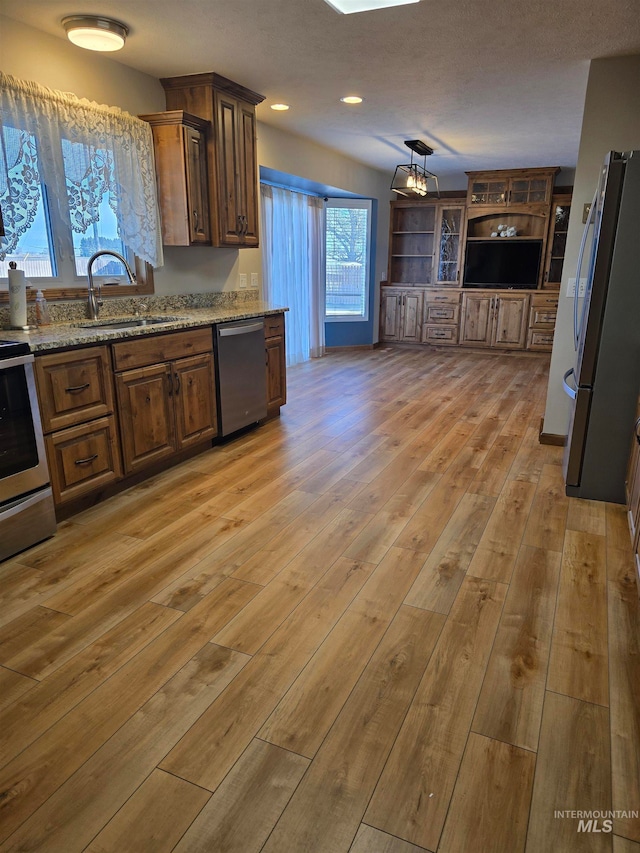 kitchen with light stone countertops, sink, light hardwood / wood-style flooring, and appliances with stainless steel finishes