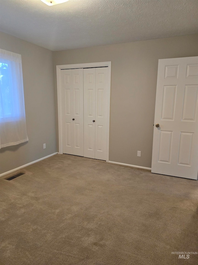 unfurnished bedroom with a textured ceiling, light carpet, and a closet