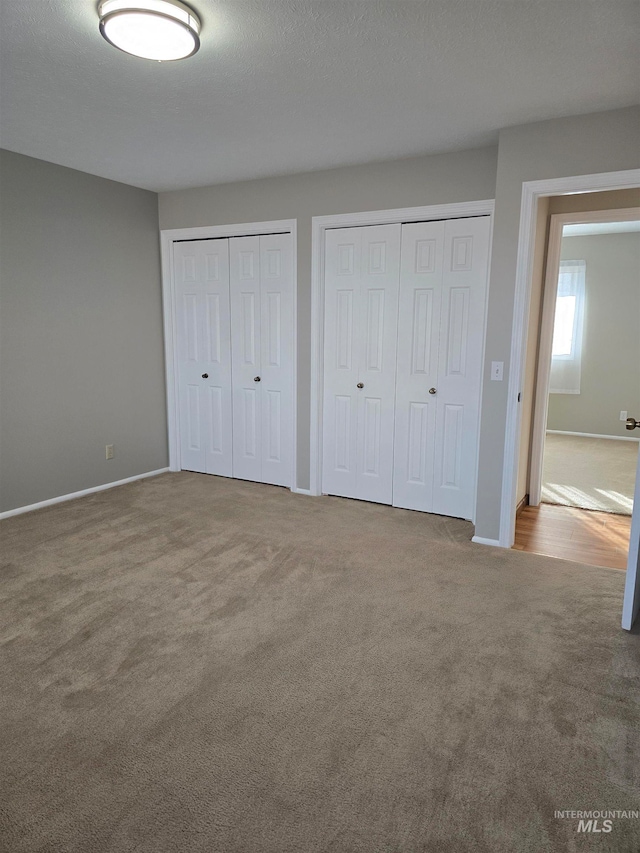 unfurnished bedroom with a textured ceiling, carpet floors, and two closets