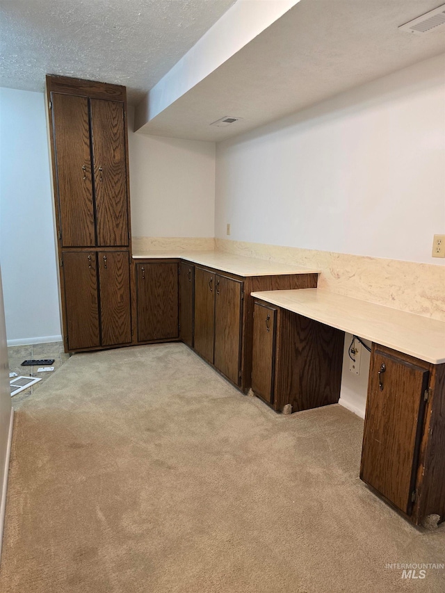 kitchen with light carpet, dark brown cabinets, and a textured ceiling