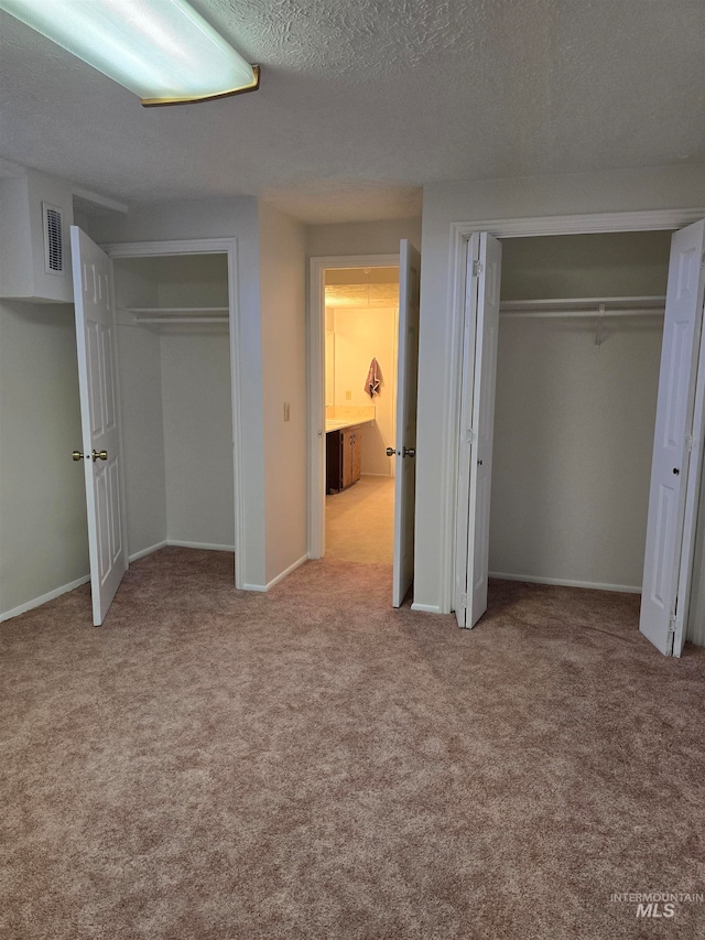 unfurnished bedroom with multiple closets, light colored carpet, and a textured ceiling