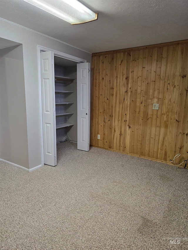 unfurnished bedroom with a textured ceiling, carpet floors, a closet, and wooden walls