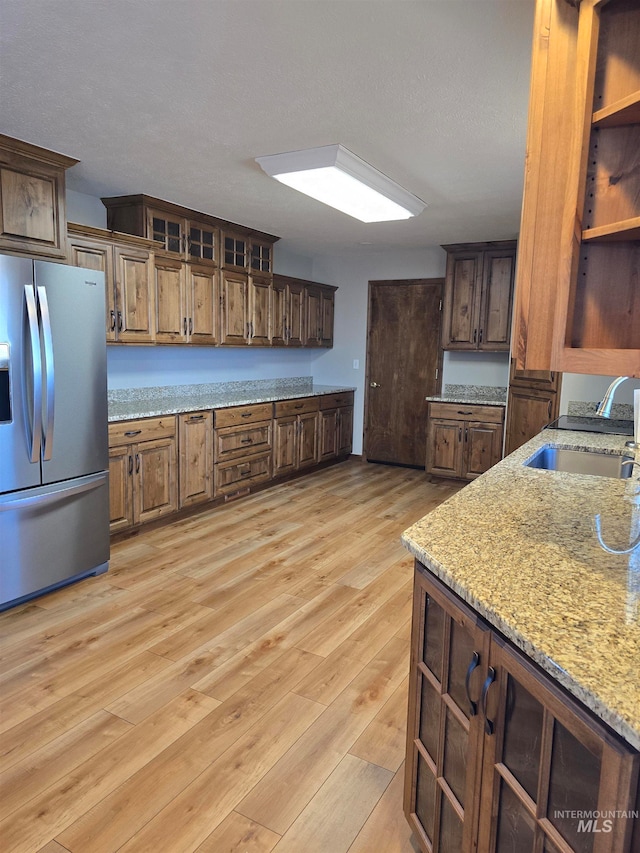 kitchen with stainless steel fridge with ice dispenser, sink, light stone counters, and light hardwood / wood-style flooring