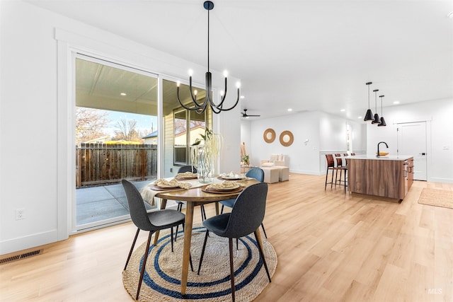 dining room featuring sink, ceiling fan with notable chandelier, and light wood-type flooring