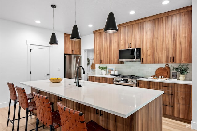 kitchen with backsplash, stainless steel appliances, sink, decorative light fixtures, and light hardwood / wood-style floors