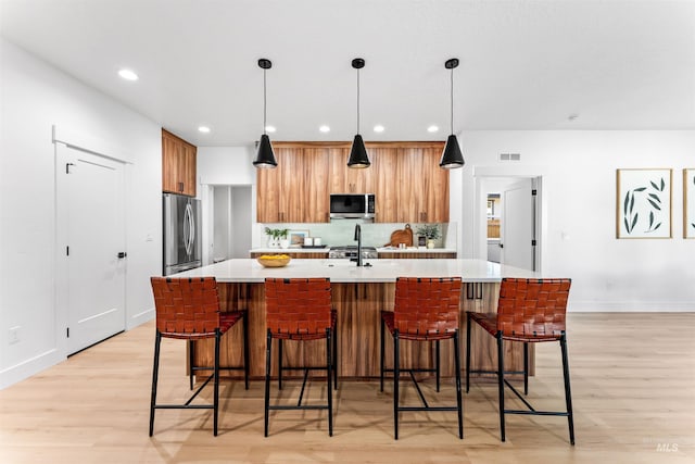 kitchen featuring pendant lighting, stainless steel appliances, light hardwood / wood-style floors, and an island with sink