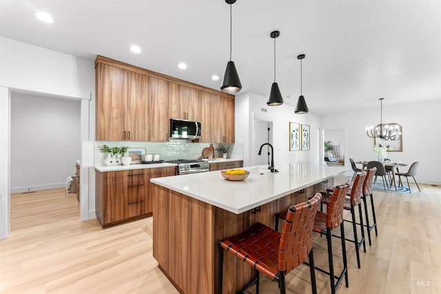 kitchen featuring hanging light fixtures, light hardwood / wood-style floors, stainless steel appliances, and a kitchen island with sink