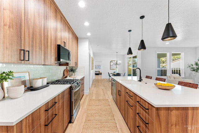 kitchen featuring decorative backsplash, light hardwood / wood-style floors, stainless steel appliances, and a large island with sink