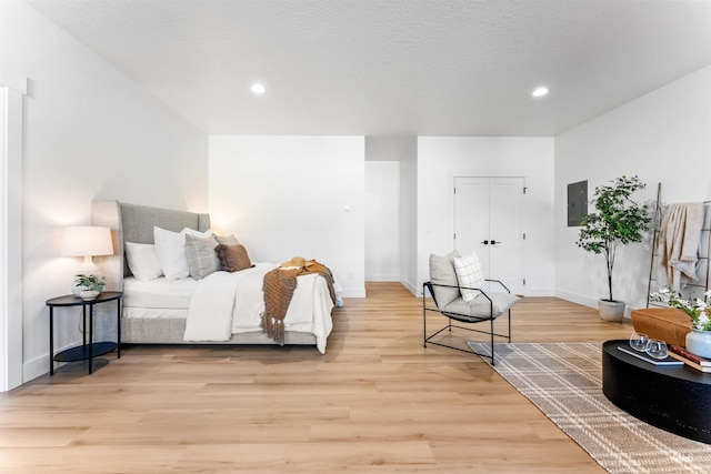 bedroom featuring electric panel, light hardwood / wood-style flooring, and a textured ceiling