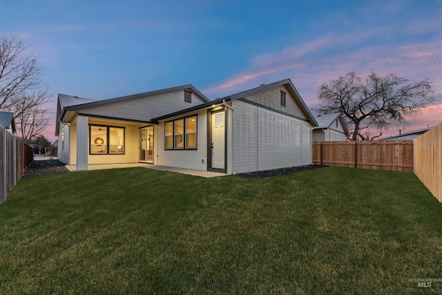 back house at dusk featuring a lawn