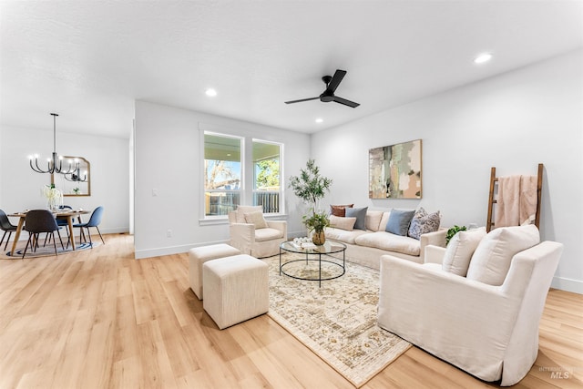 living room featuring ceiling fan with notable chandelier and light wood-type flooring