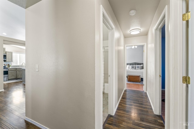 corridor featuring a sink, baseboards, and dark wood-type flooring