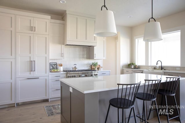 kitchen with a sink, decorative backsplash, light wood-style floors, a breakfast bar area, and light countertops