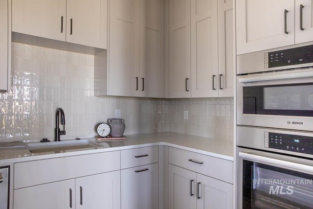 kitchen featuring double oven, tasteful backsplash, light countertops, and a sink