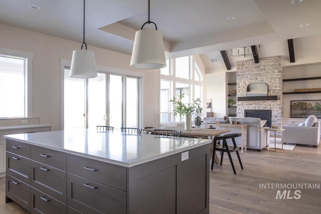 kitchen with light wood-type flooring, visible vents, a stone fireplace, light countertops, and gray cabinetry